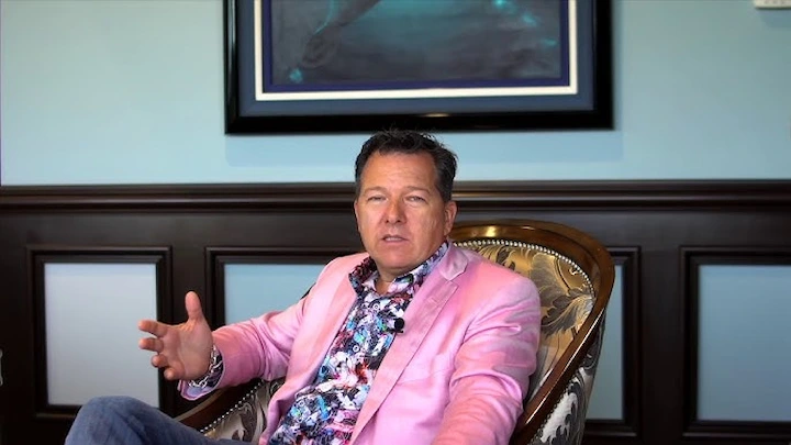 Chuck Whittall in a pink blazer speaking during an interview at his office.