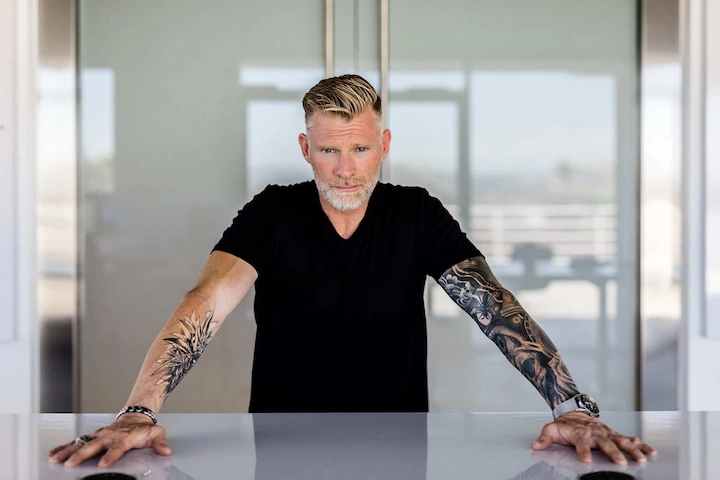 Garrett J. White standing confidently with tattooed arms resting on a countertop, symbolizing strength and leadership.